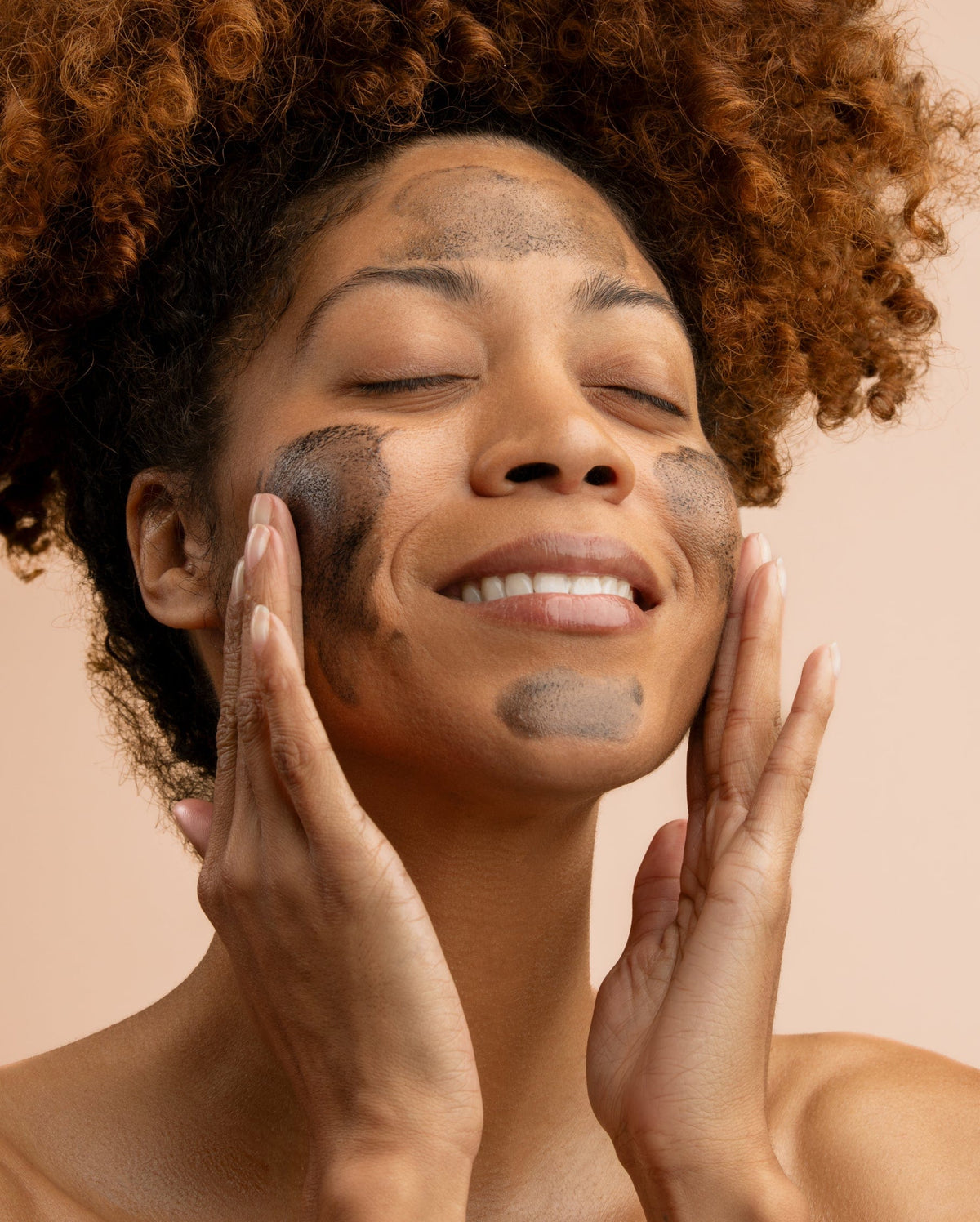 Bambu Earth Activated Charcoal Cleansing Oil - A close-up of a woman with curly brown hair smiling while applying or washing