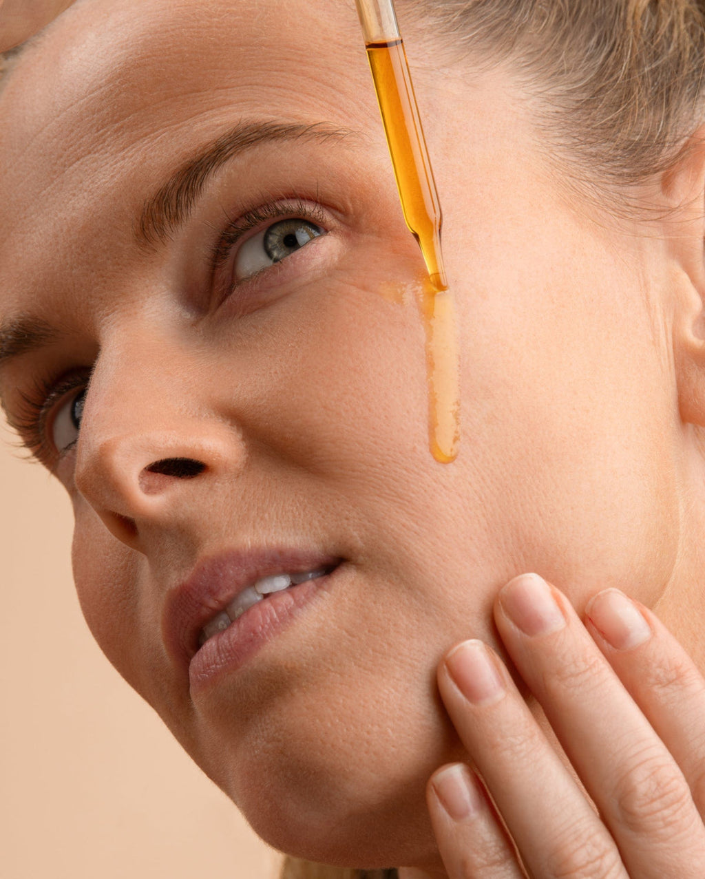 Bambu Earth Rosehip Repairing Facial Serum - Close-up of a woman's face with a glass dropper applying an amber-colored